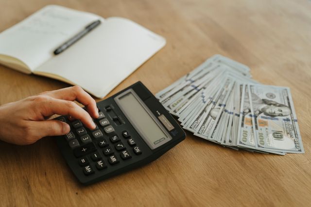 A property owner using a calculator and a notebook to budget next to cash