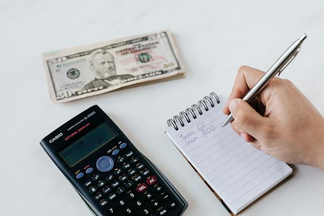 hand holding a pen and calculator next to notepad and money